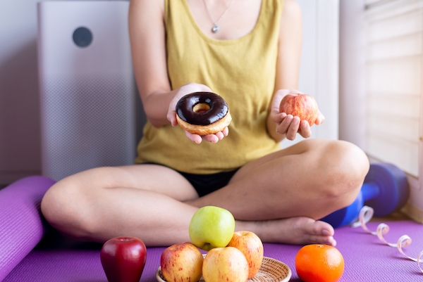 Hypnose zum Abnehmen: Frau hält Donut und Apfel in den Händen und wägt ab